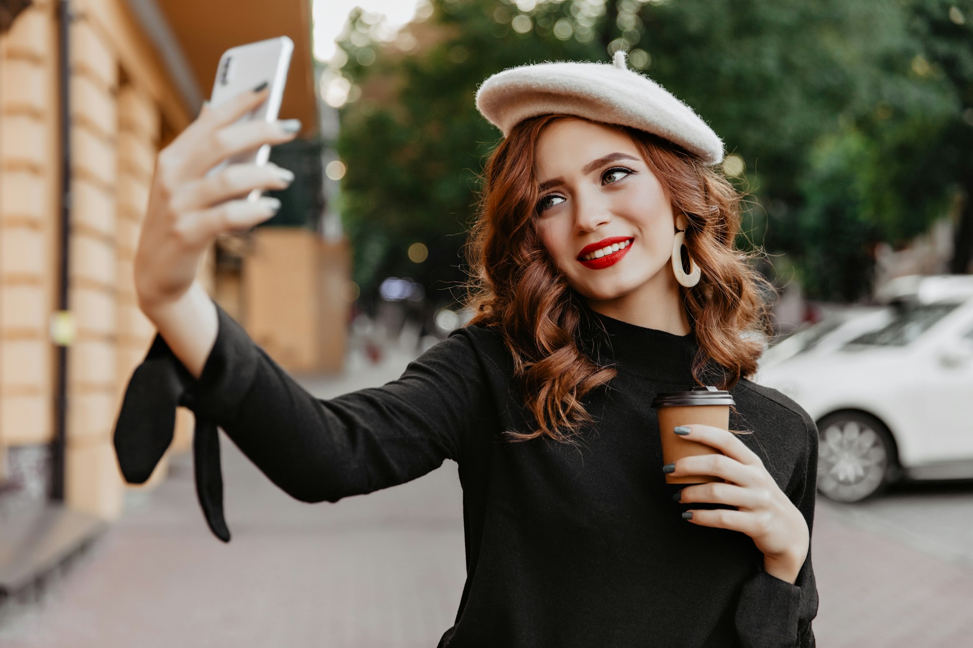 A woman in a beret taking a selfie with a coffee cup