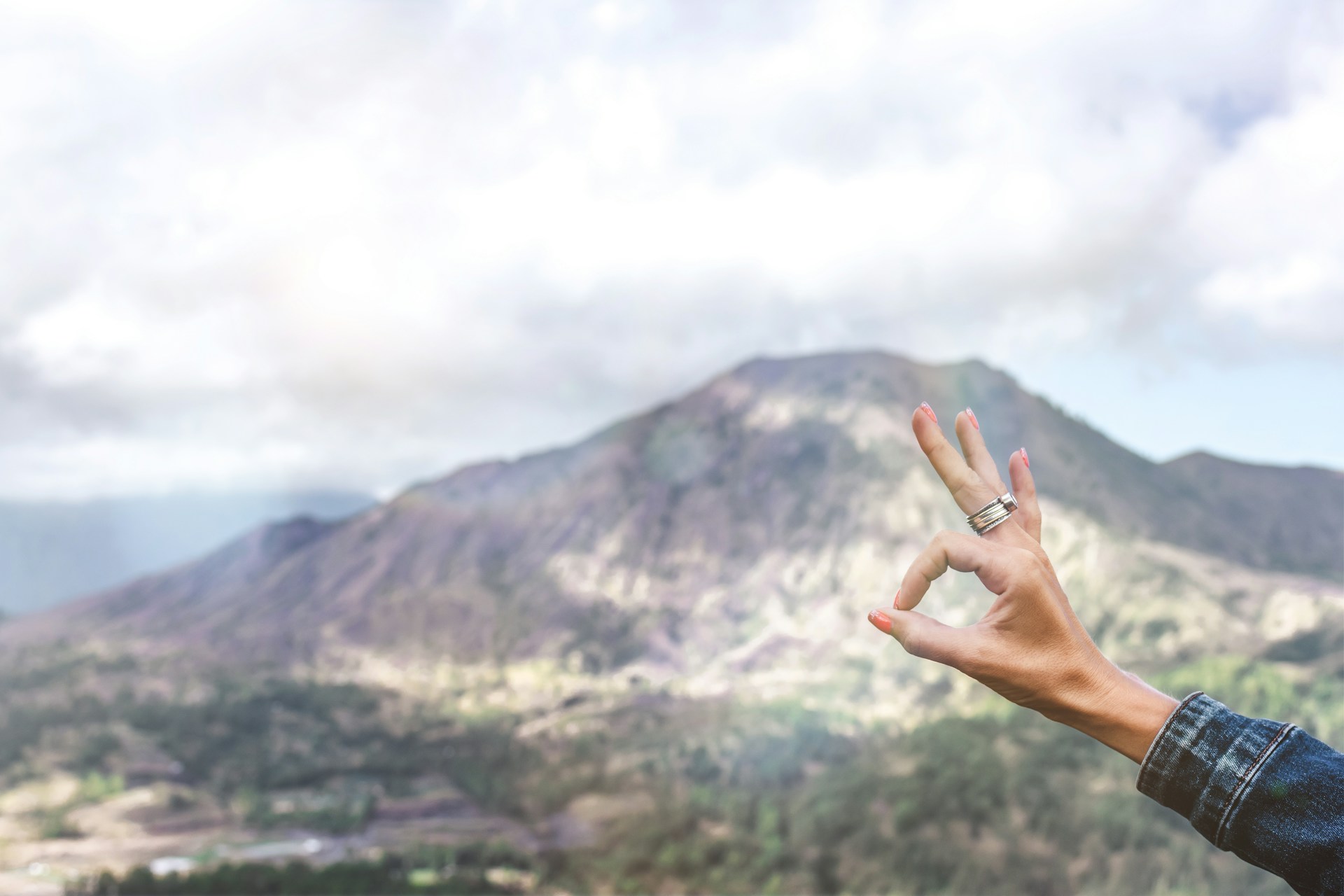 A hand making an 'OK' sign against a mountain backdrop