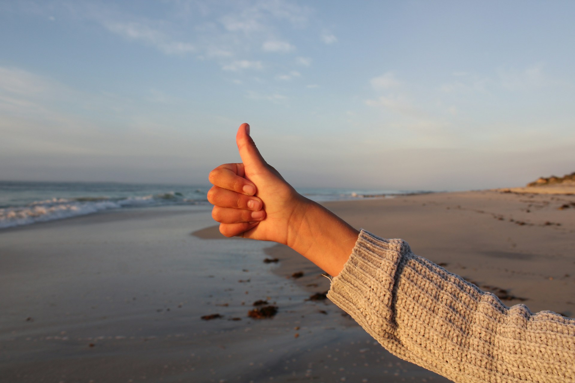 A person showing thumbs up on a beach