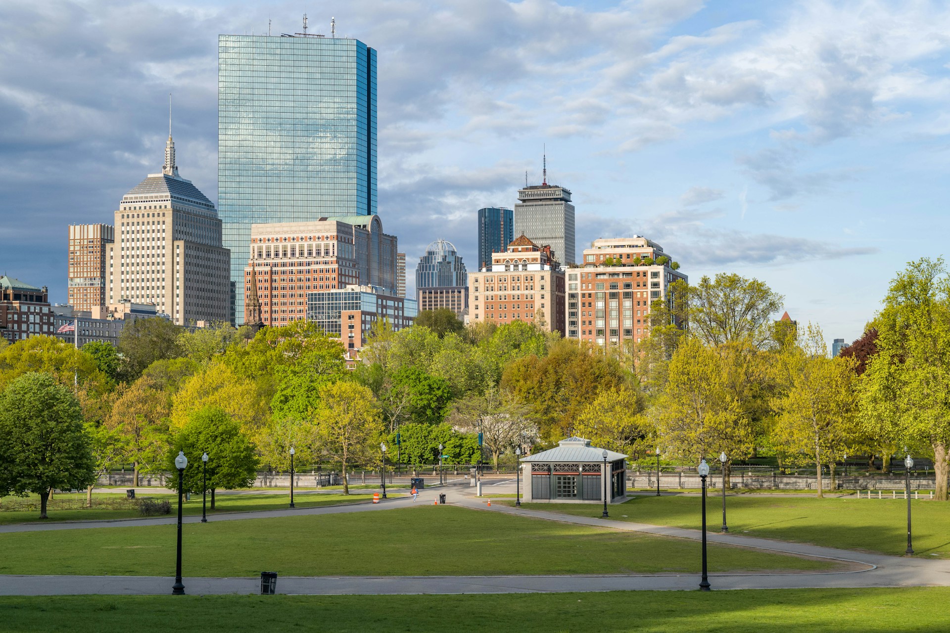 green grass field with trees and buildings in distance under white clouds and blue sky