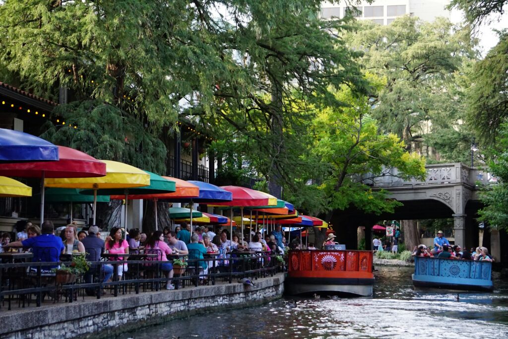 A group of people sitting under umbrellas on the side of a river